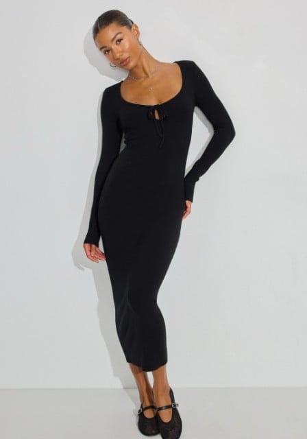 Model poses in a long sleeve black midi dress.