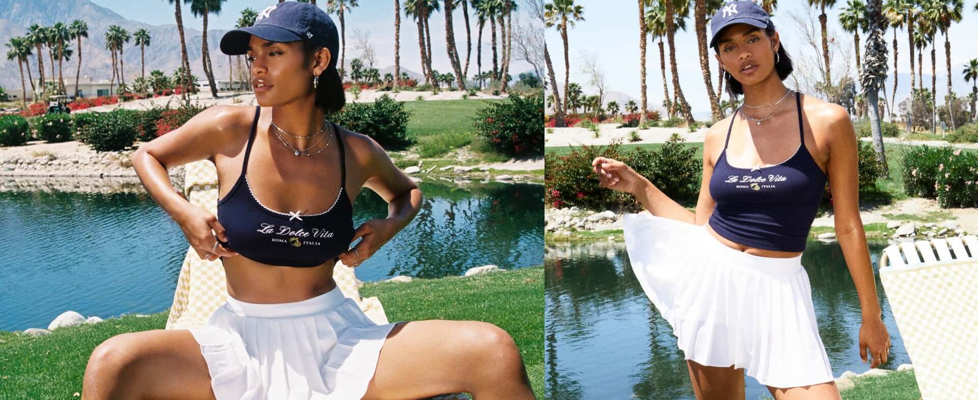 Model poses by a lake wearing a graphic tank top, a white skirt, and a navy cap.