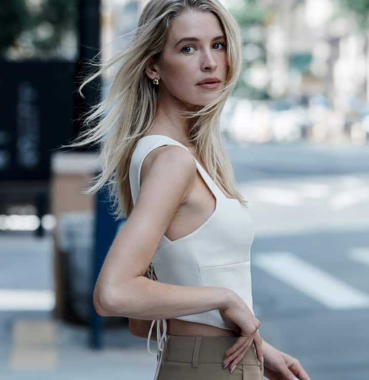 La mannequin porte une camisole blanche et un pantalon brun.