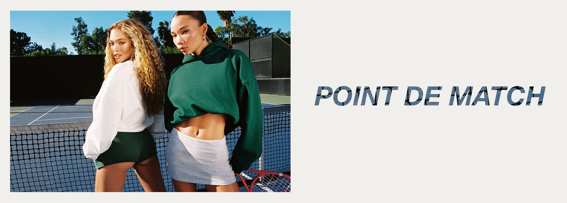 Deux mannequins pennent la pose sur un terrain de tennis : l'une porte un sweatshirt blanc et un short vert, l'autre porte un haut à capuchon vert et une jupe blanche.