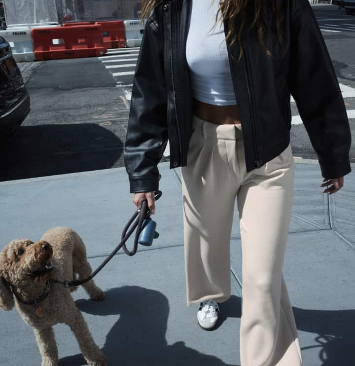 La mannequin porte un blouson en faux cuir noir par-dessus un t-shirt blanc et un pantalon beige.