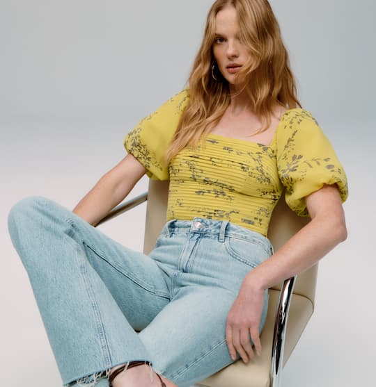 La mannequin porte un haut jaune à manches bouffantes et un jean bleu.