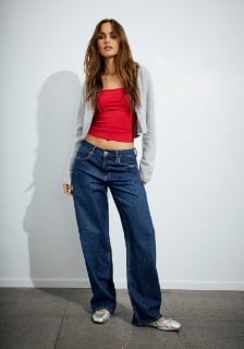 Model wears a grey cardigan, a red tank top, and dark wash baggy jeans.