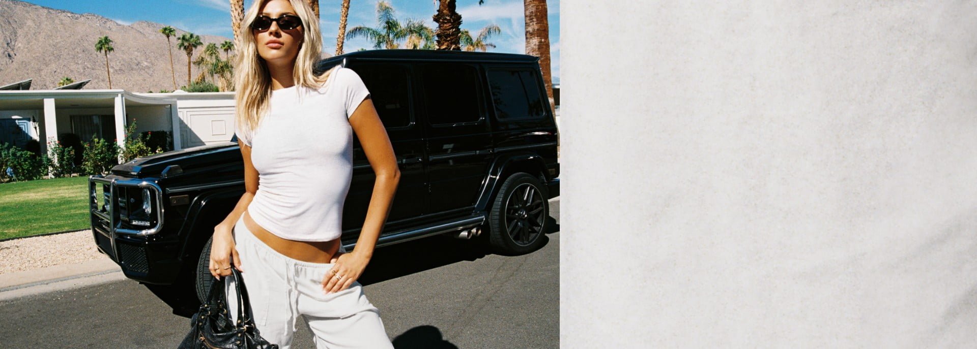 Model poses by a car in a white t-shirt and cream sweatpants.