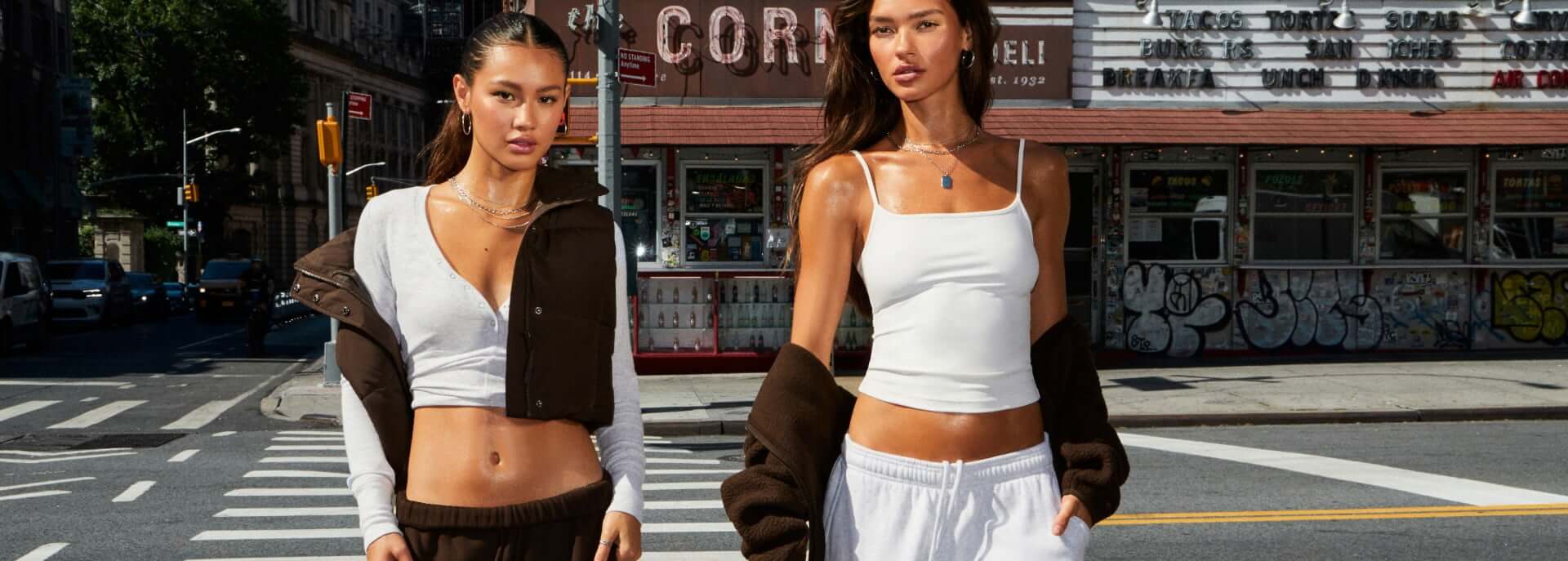 Model sits on the hood of a car in a white off the shoulder top and grey sweats.