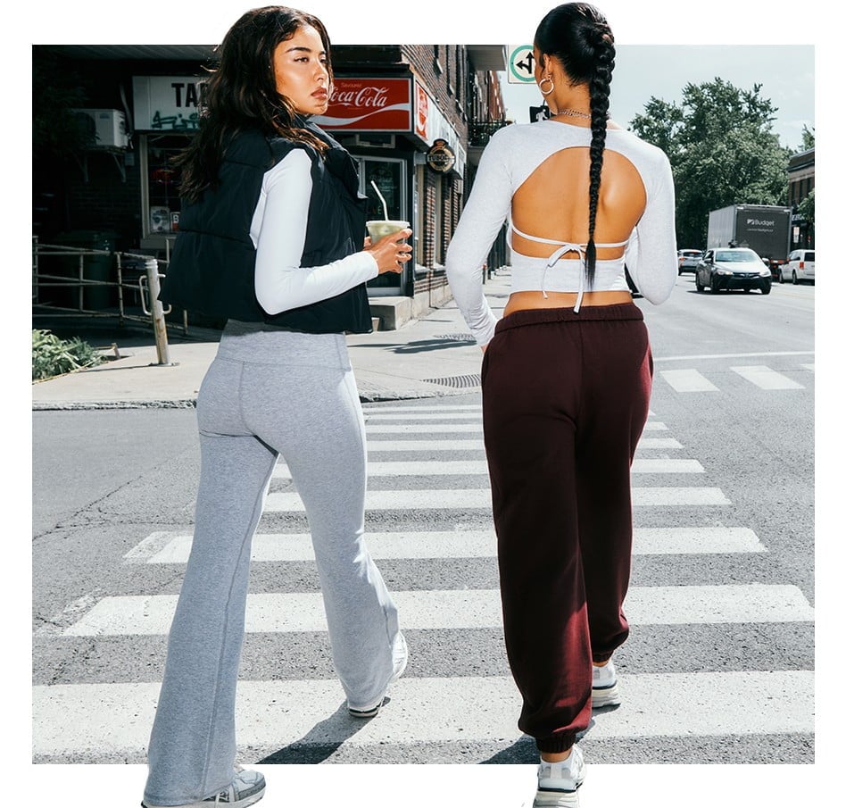 Two models cross the street. One wears a long sleeve white shirt, a black vest, and white sweats.