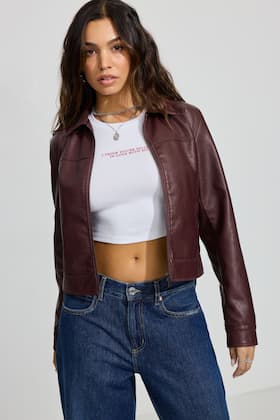 Model wears a brown faux leather jacket with a cropped t-shirt and jeans.