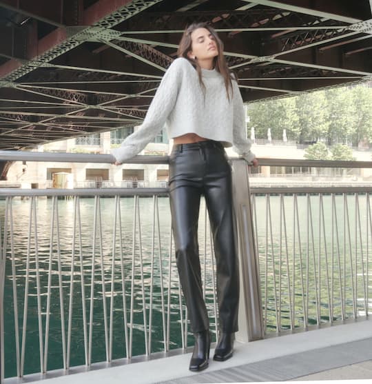 Model is wearing grey sweater and black faux-leather pants.