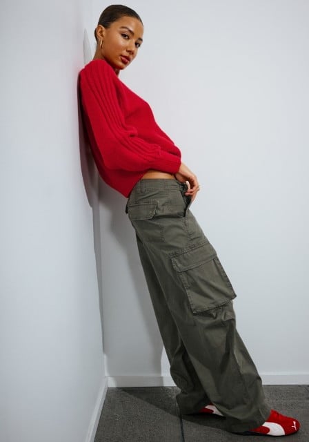 Model leaning in a red long sleeve sweater and grey cargo pants.