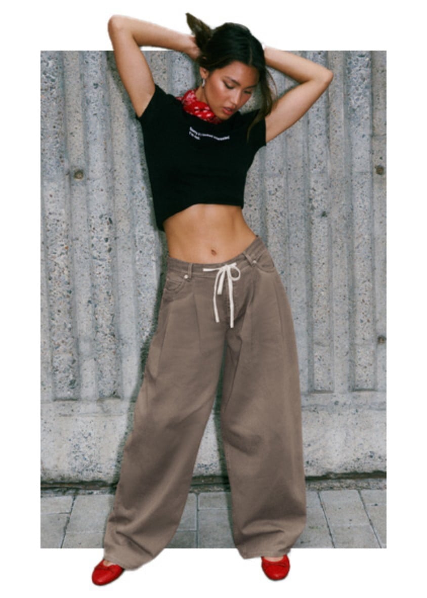 Model poses in a black graphic tshirt and baggy brown pants.