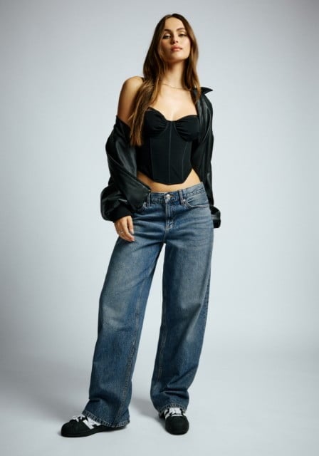 Model wears a black leather jacket, a black bustier top, and baggy mid-wash jeans.