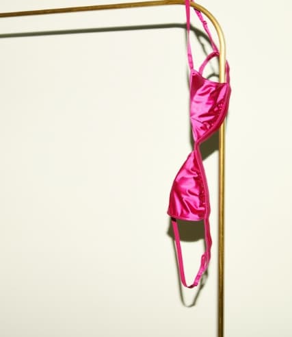 Pink satin bralette hanging off rack.