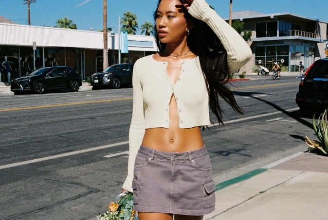 Model poses on a sidewalk wearing a white cardigan with no shirt underneath and a grey cargo skirt.