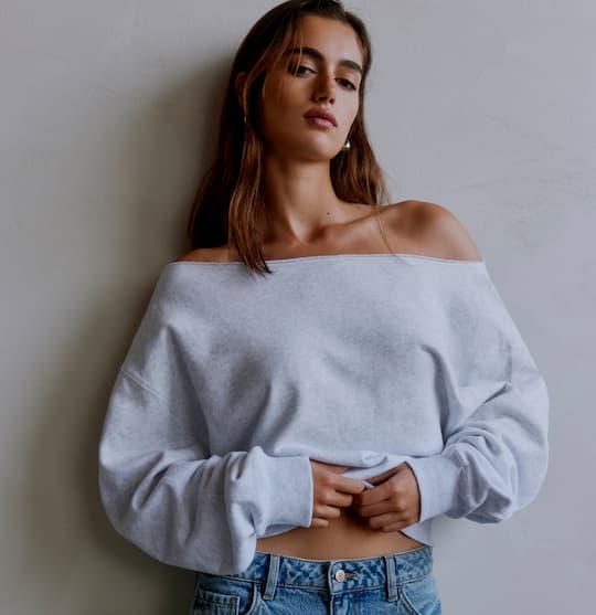 Model is wearing grey off-shoulder sweater and blue jeans on sale.