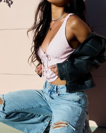 Model poses wearing a lilac tank top, light wash jeans, and a faux leather jacket.