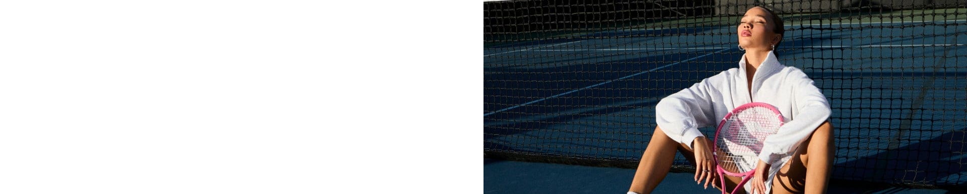 Two models pose on a tennis court, one with a water bottle, wearing a navy tank top with a white trim and black pants, the other in a white polo and light grey sweats.