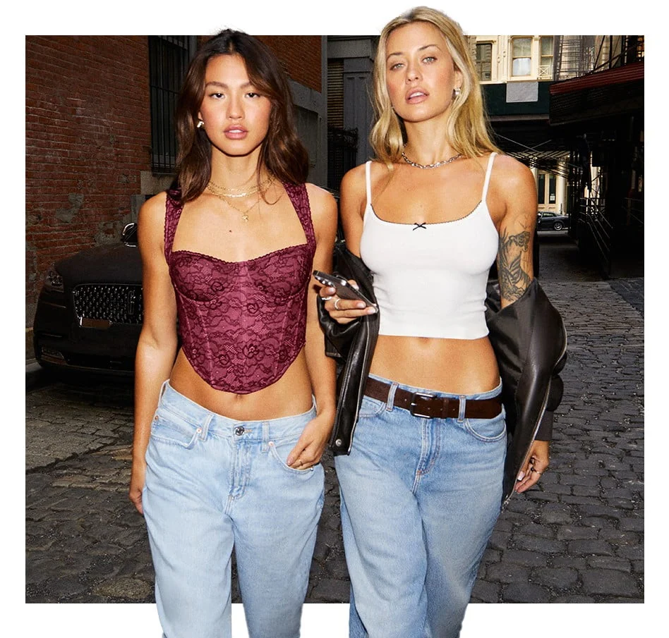 Two models walk down the street. One wears a burgundy corset top and light wash baggy jeans.